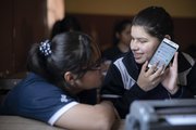 Two students in the classroom are using a phone.