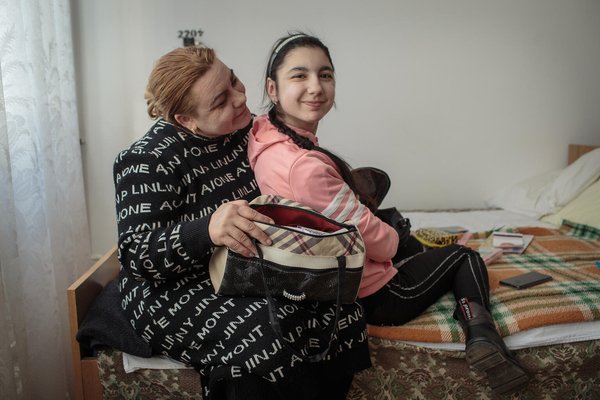 A mother is sitting next to her child with a disability in bed.