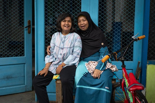 A mother is sitting next to her child with a disability.